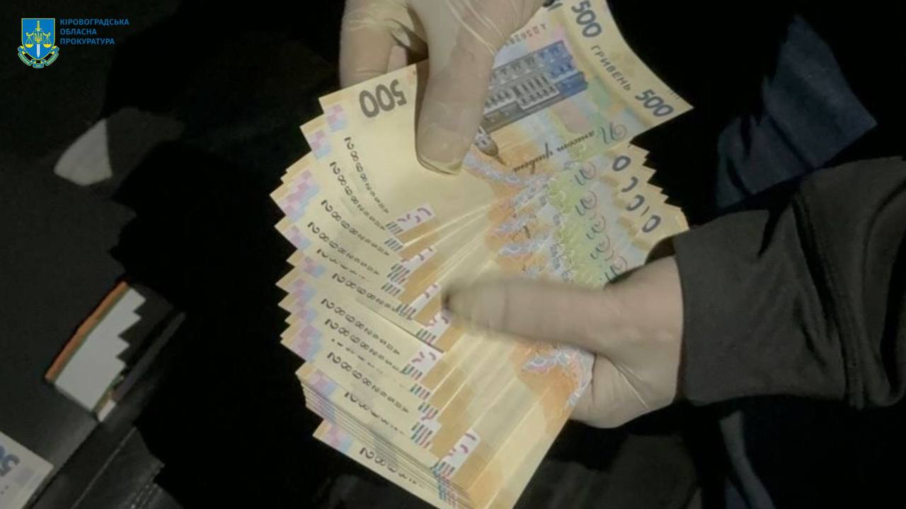 Рука, що тримає пачку банкнот номіналом 500 гривень. Рука одягнена в рукавичку.