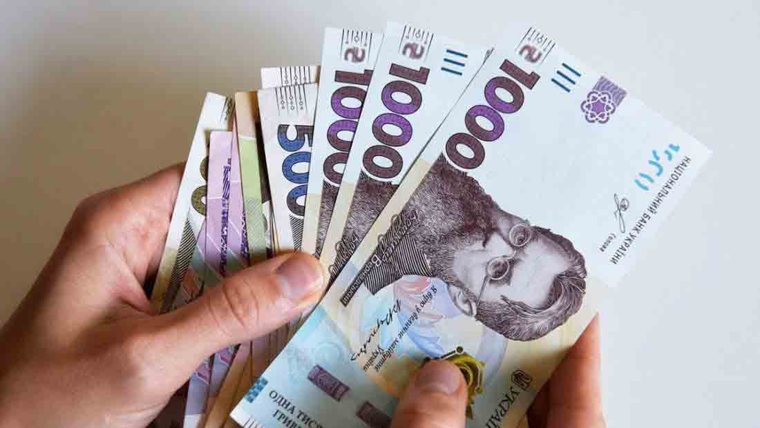 Руки тримають пачку українських купюр. Видно банкноти номіналом 1000 та 500 гривень. Банкнота номіналом 1000 гривень має зображення відомого українського діяча.