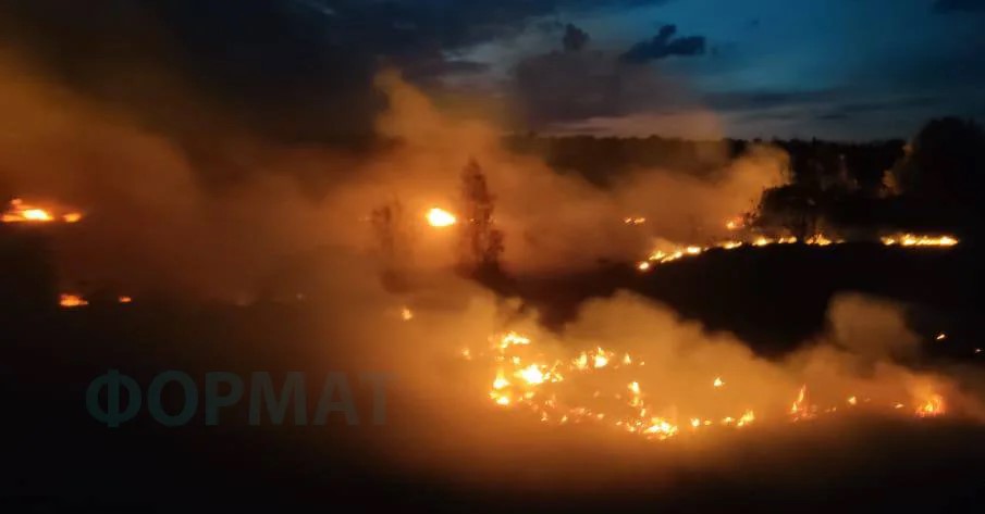 Поле, охоплене вогнем. Полум'я поширюється вздовж землі, створюючи лінії вогню. Задній план затемнений, що свідчить про нічний час чи вечір. Над полем піднімаються густі хмари диму.